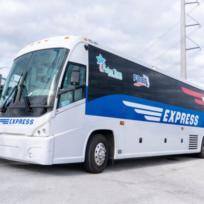 White and blue Express bus parked near a shelter, under a cloudy sky. Logos for transportation services displayed. The mood is calm and professional.