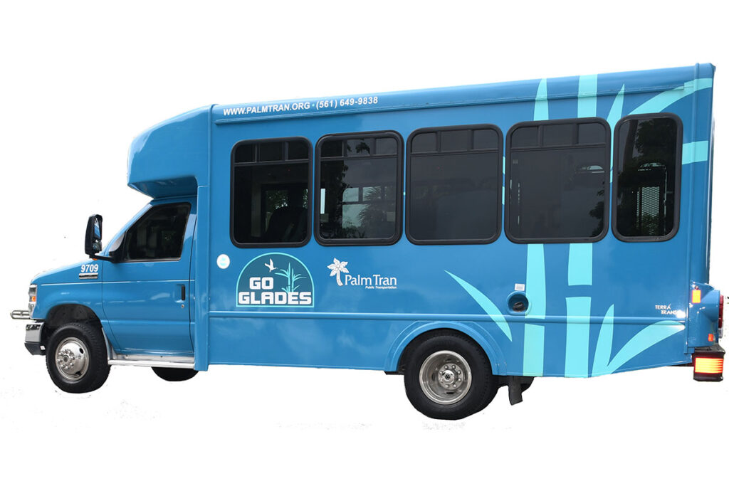 Blue Go Glades shuttle bus with Palm Tran branding, featuring large windows and graphic designs of trees. The bus has a cheerful, modern look.